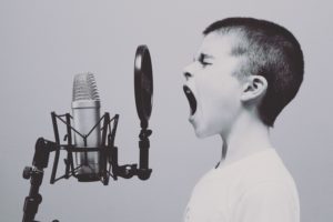 Person singing into a microphone with hand raised, mid-performance